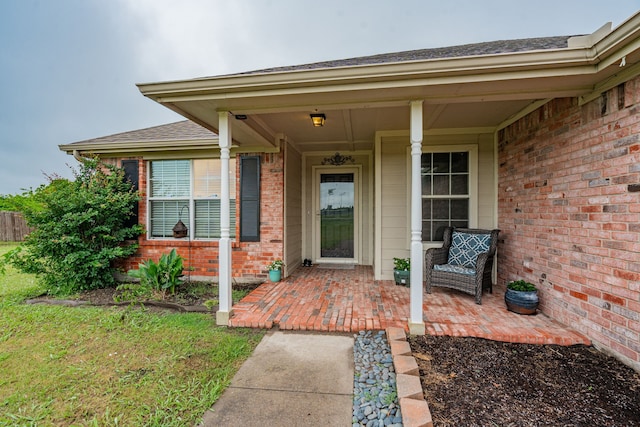entrance to property with brick siding, a shingled roof, and a patio
