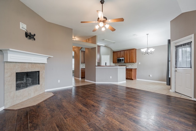 unfurnished living room with ceiling fan with notable chandelier, a fireplace, vaulted ceiling, and light wood-style flooring