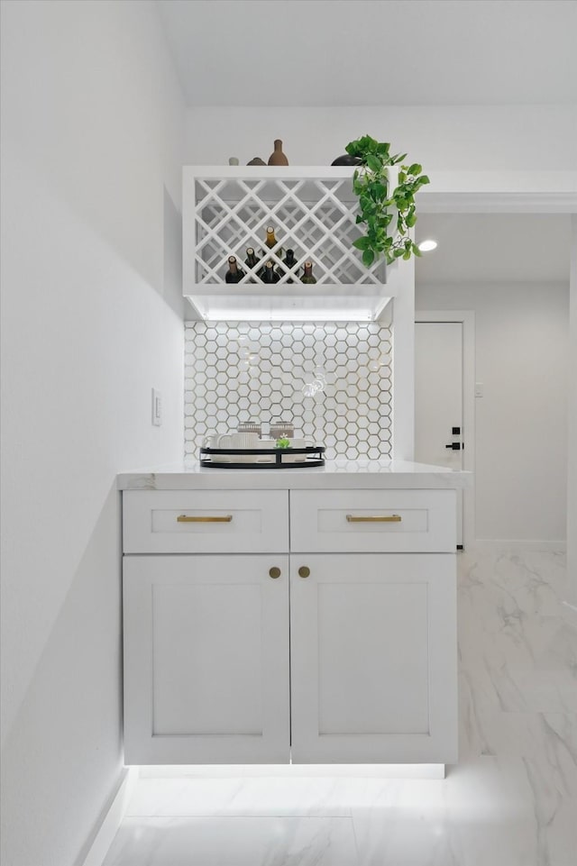 indoor bar with light marble finish floors, decorative backsplash, cooktop, and baseboards