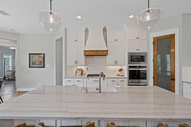 kitchen with white cabinets, appliances with stainless steel finishes, premium range hood, a large island, and backsplash