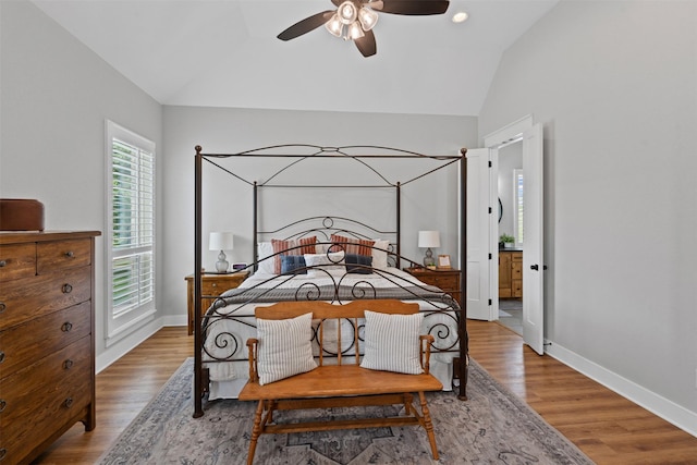 bedroom with baseboards, ensuite bath, wood finished floors, and vaulted ceiling