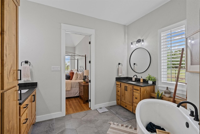 ensuite bathroom featuring two vanities, tile patterned floors, a soaking tub, a sink, and ensuite bath