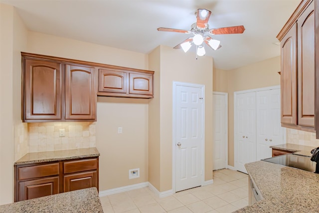 kitchen with light stone countertops, baseboards, a ceiling fan, backsplash, and light tile patterned floors
