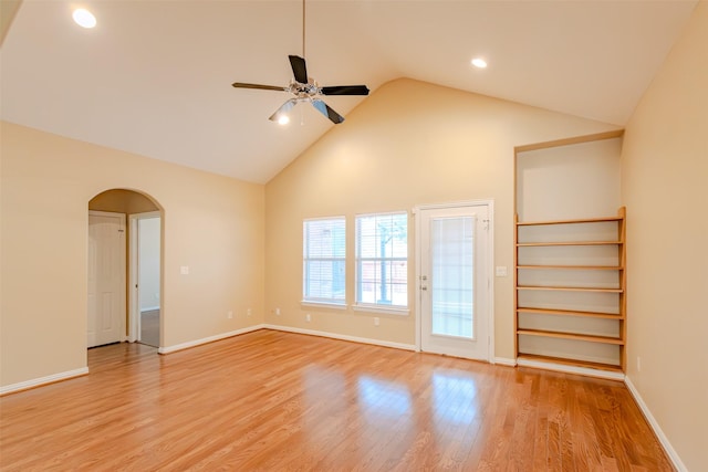 empty room featuring a ceiling fan, arched walkways, baseboards, high vaulted ceiling, and light wood finished floors
