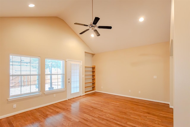 spare room featuring light wood-type flooring, a ceiling fan, baseboards, and high vaulted ceiling