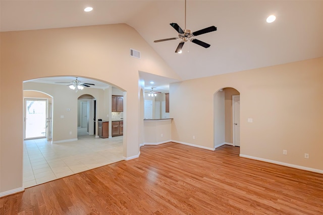 unfurnished room featuring arched walkways, high vaulted ceiling, a ceiling fan, light wood-type flooring, and visible vents