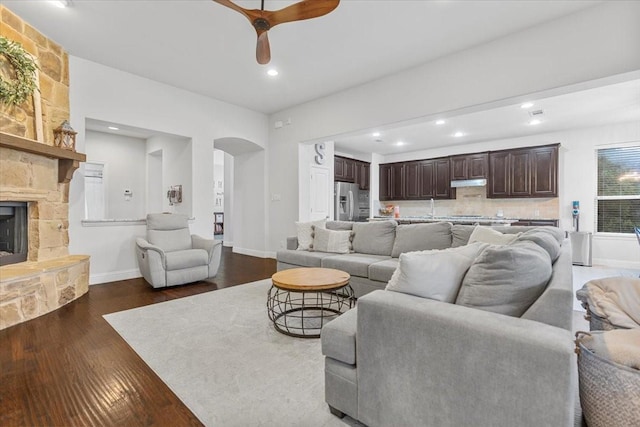 living area with a fireplace, dark wood-type flooring, recessed lighting, arched walkways, and a ceiling fan