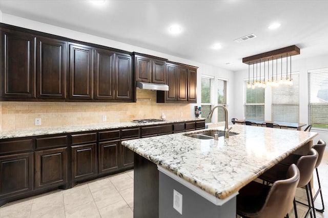kitchen with a sink, a breakfast bar area, stainless steel gas cooktop, decorative backsplash, and visible vents