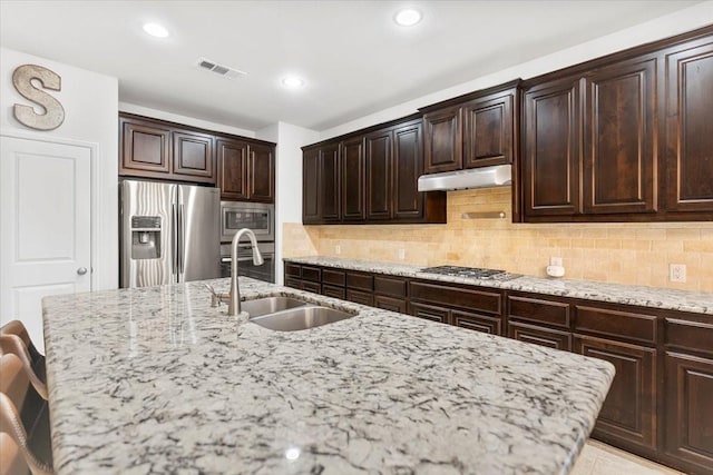 kitchen featuring light stone countertops, appliances with stainless steel finishes, a sink, under cabinet range hood, and visible vents