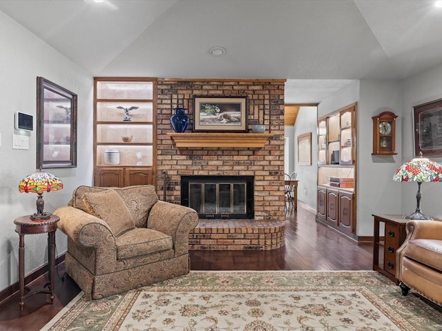 living area with a brick fireplace, built in features, baseboards, wood finished floors, and lofted ceiling