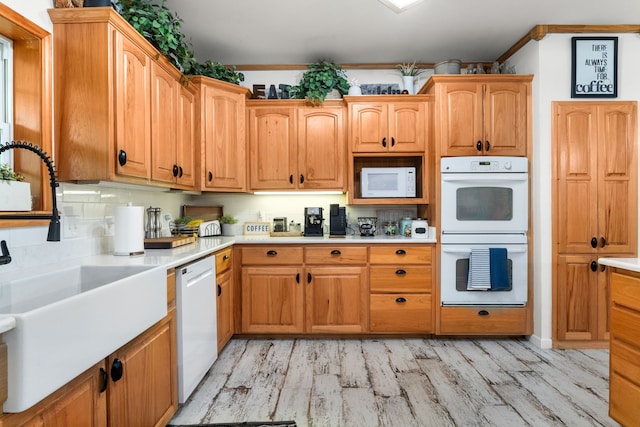 kitchen featuring a sink, light countertops, ornamental molding, white appliances, and light wood-style flooring