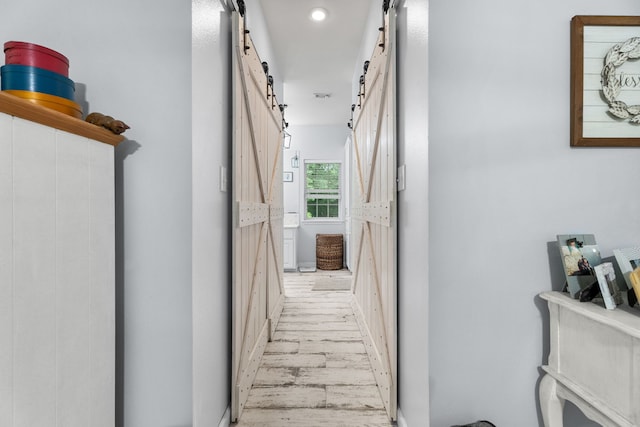 hallway with light wood-style floors, recessed lighting, and a barn door