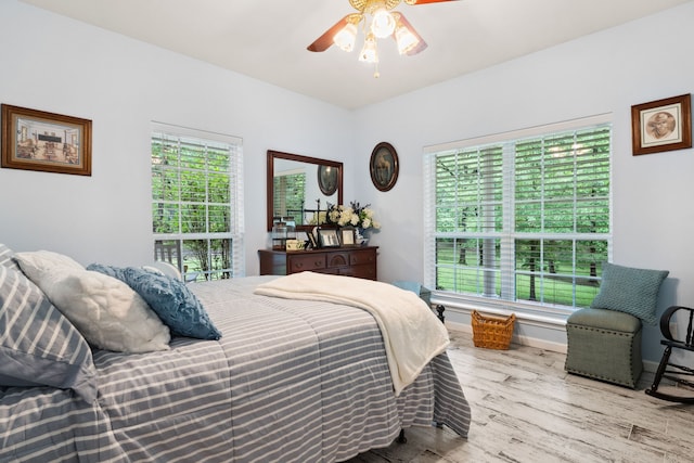 bedroom featuring baseboards, multiple windows, a ceiling fan, and wood finished floors