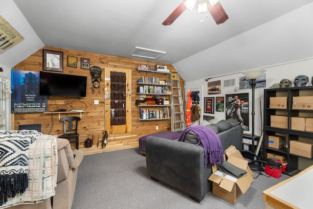 carpeted living area with wooden walls, ceiling fan, attic access, and lofted ceiling