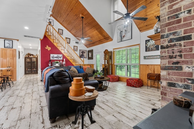 living room featuring ceiling fan, wood finished floors, stairway, high vaulted ceiling, and a wainscoted wall