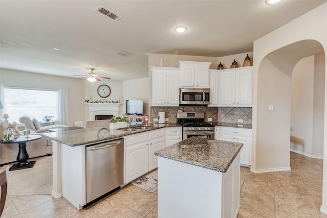 kitchen featuring visible vents, a peninsula, open floor plan, arched walkways, and appliances with stainless steel finishes