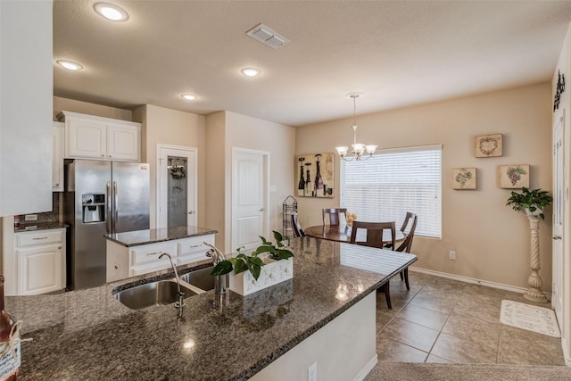 kitchen featuring visible vents, a sink, a chandelier, stainless steel fridge, and white cabinetry