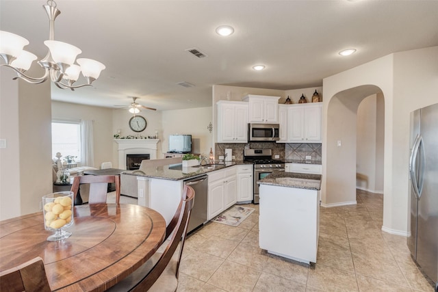 kitchen with white cabinets, ceiling fan with notable chandelier, stainless steel appliances, a peninsula, and tasteful backsplash