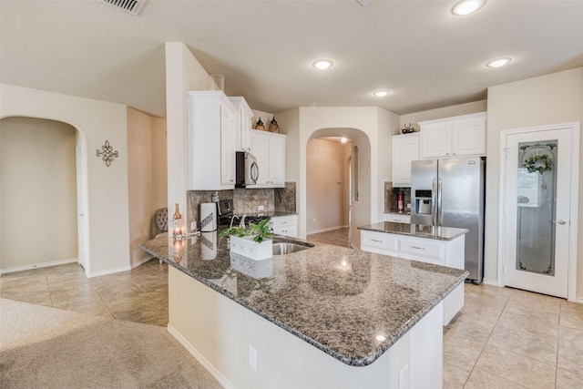 kitchen with arched walkways, appliances with stainless steel finishes, a sink, dark stone countertops, and a peninsula