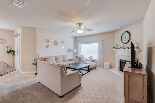 carpeted living room featuring baseboards, a fireplace with raised hearth, a ceiling fan, and visible vents