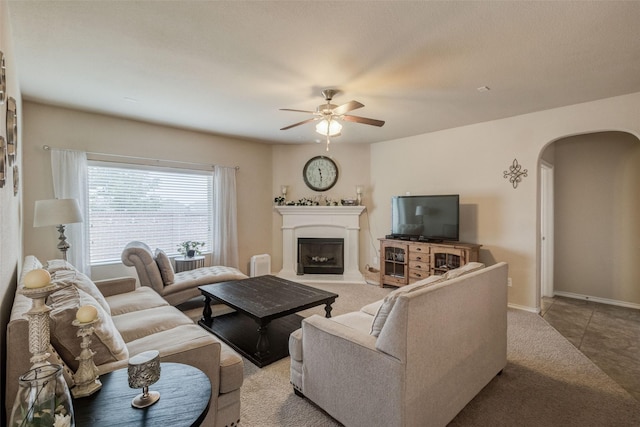 living room featuring a ceiling fan, carpet flooring, a fireplace, baseboards, and arched walkways