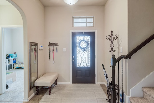foyer entrance with baseboards, arched walkways, stairs, and carpet flooring