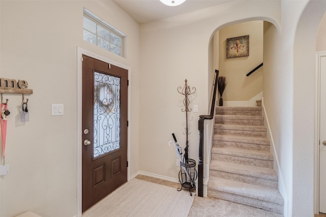 entryway featuring arched walkways, baseboards, and stairs