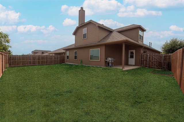 back of house featuring a lawn, a chimney, a fenced backyard, and a patio area
