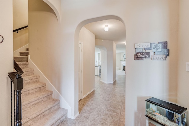 hallway featuring baseboards, arched walkways, light tile patterned floors, and stairway