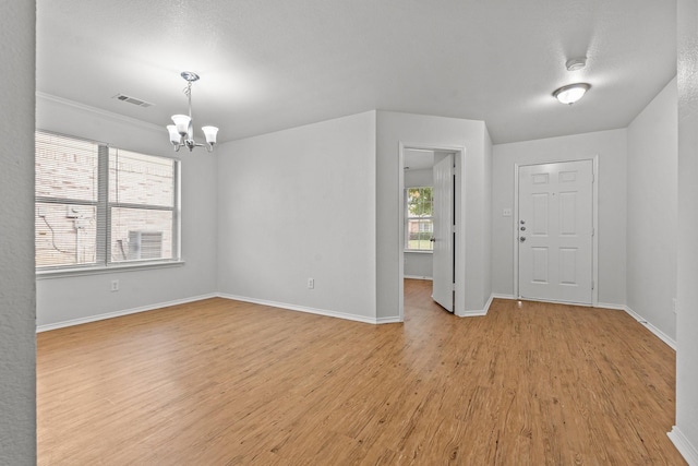 unfurnished room featuring an inviting chandelier, baseboards, light wood-type flooring, and visible vents