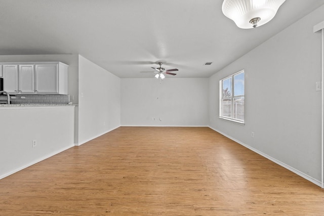 unfurnished living room featuring visible vents, a sink, baseboards, a ceiling fan, and light wood-style flooring