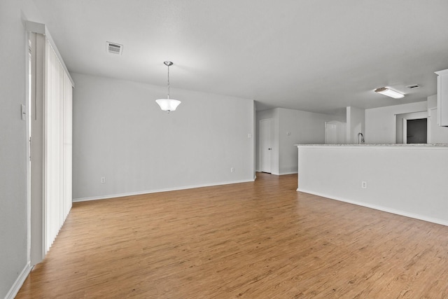 unfurnished living room with baseboards, visible vents, a sink, and light wood finished floors