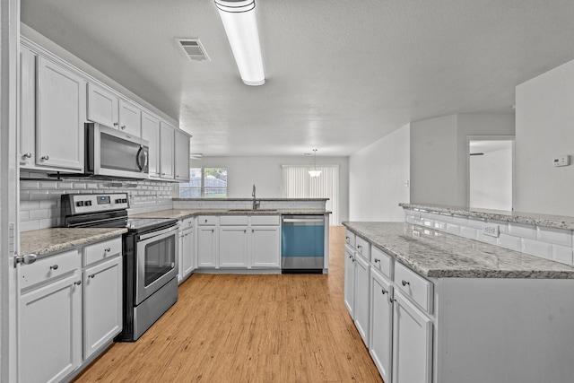 kitchen with appliances with stainless steel finishes, a sink, light wood-style floors, a peninsula, and visible vents