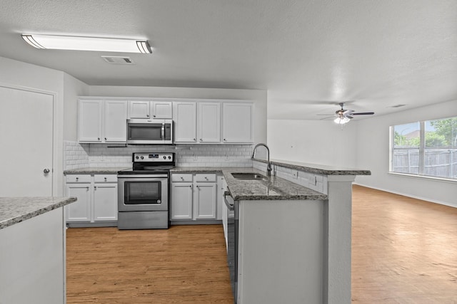 kitchen featuring a sink, stainless steel appliances, a peninsula, backsplash, and visible vents