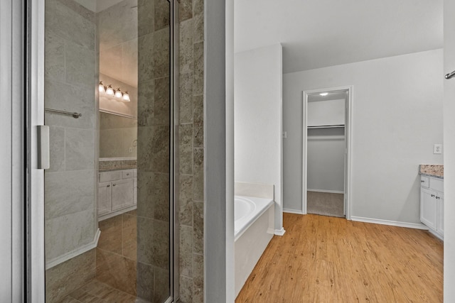 full bathroom with vanity, wood finished floors, a bath, a spacious closet, and a stall shower