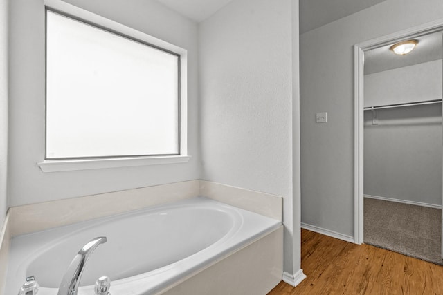 bathroom featuring a garden tub, baseboards, wood finished floors, and a spacious closet