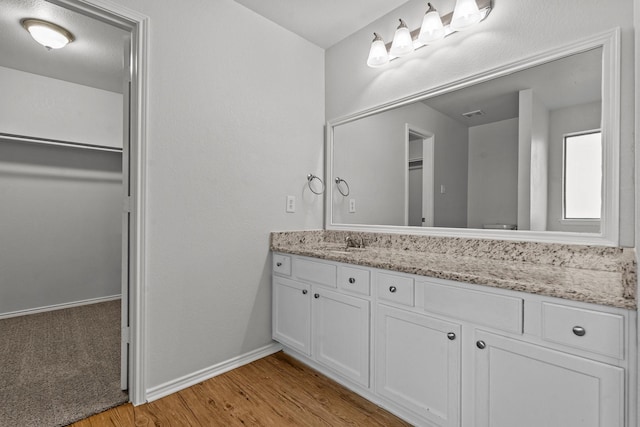 bathroom featuring vanity, baseboards, wood finished floors, and a spacious closet