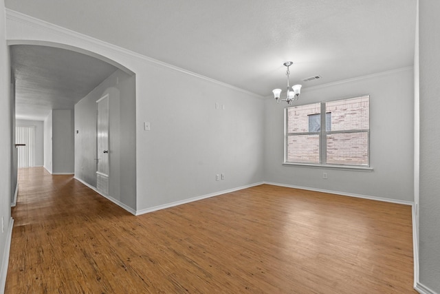 spare room with an inviting chandelier, ornamental molding, wood finished floors, baseboards, and arched walkways