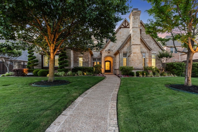 english style home featuring a chimney, a front yard, and stone siding