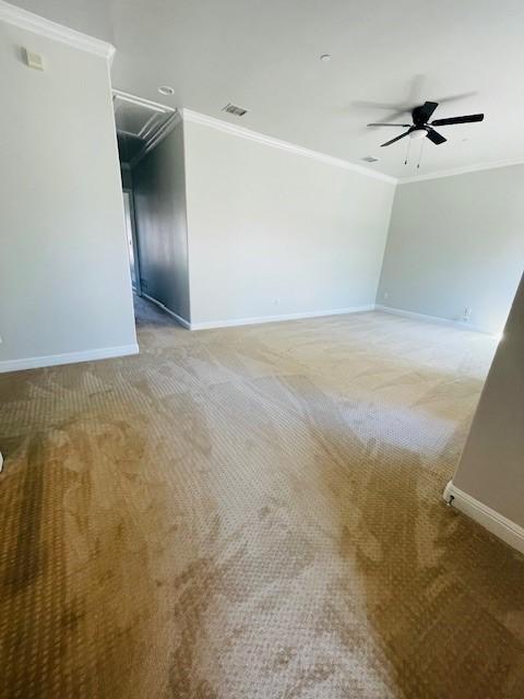 empty room featuring crown molding, ceiling fan, light colored carpet, attic access, and baseboards