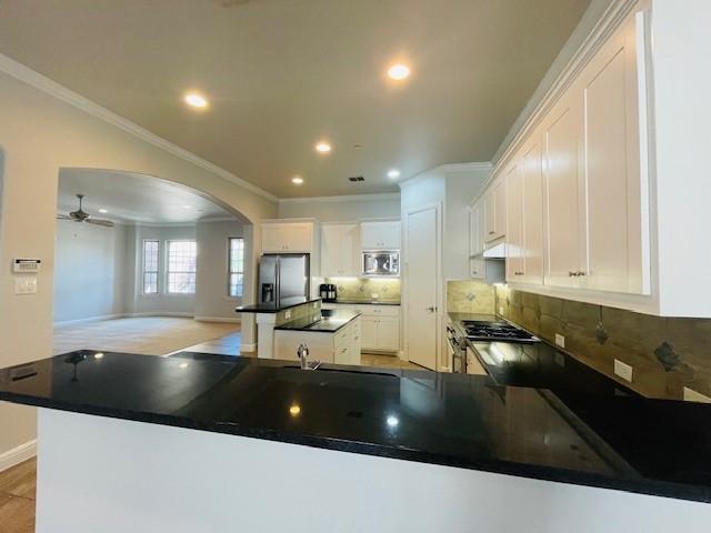 kitchen featuring crown molding, appliances with stainless steel finishes, arched walkways, decorative backsplash, and a kitchen island