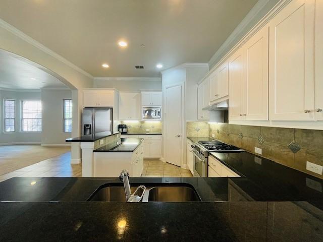 kitchen featuring appliances with stainless steel finishes, a sink, arched walkways, under cabinet range hood, and visible vents