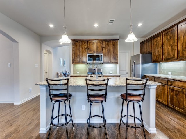 5517 Grove Cove Dr, Mckinney, TX 75071 - kitchen with a kitchen island with sink, backsplash, arched walkways, dark wood-style floors, and stainless steel appliances