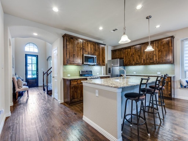 5517 Grove Cove Dr, Mckinney, TX 75071 - kitchen with decorative backsplash, appliances with stainless steel finishes, arched walkways, a center island with sink, and dark wood finished floors