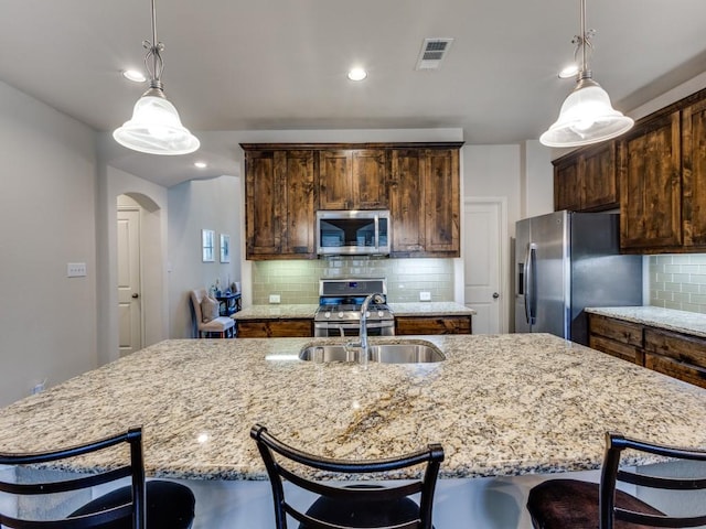 5517 Grove Cove Dr, Mckinney, TX 75071 - kitchen featuring appliances with stainless steel finishes, light stone counters, arched walkways, tasteful backsplash, and visible vents