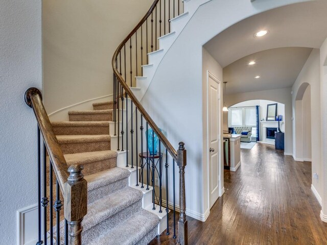 5517 Grove Cove Dr, Mckinney, TX 75071 - stairs with arched walkways, recessed lighting, a glass covered fireplace, and wood finished floors