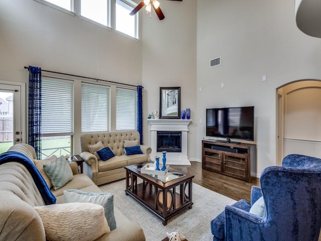 5517 Grove Cove Dr, Mckinney, TX 75071 - living room featuring visible vents, a glass covered fireplace, wood finished floors, ceiling fan, and a high ceiling