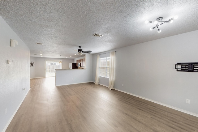unfurnished living room featuring visible vents, baseboards, a textured ceiling, and wood finished floors