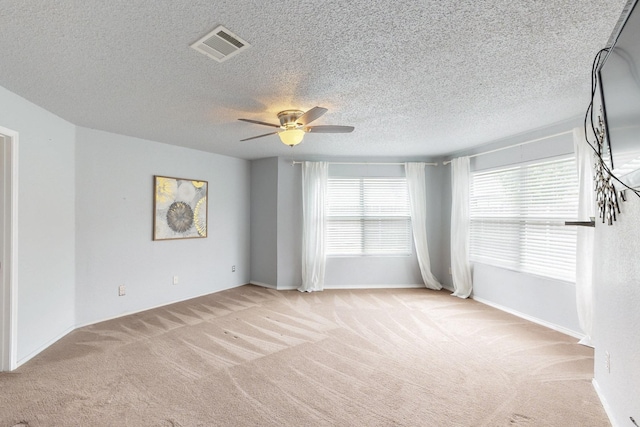 spare room with visible vents, baseboards, ceiling fan, light colored carpet, and a textured ceiling