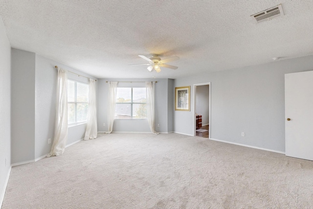 carpeted spare room with baseboards, ceiling fan, a textured ceiling, and visible vents